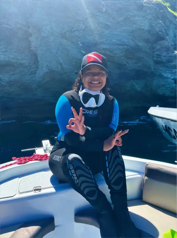 Plongeuse souriante sur un bateau, faisant un signe de paix