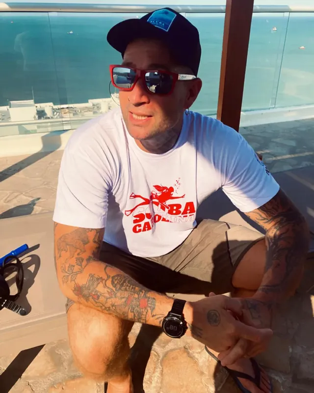 Homme tatoué portant un t-shirt de plongée et des lunettes de soleil