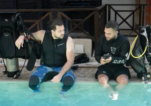 Deux plongeurs assis au bord d'une piscine vérifient leur équipement