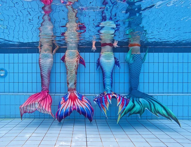 Quatre personnes en sirène nagent sous l'eau dans une piscine