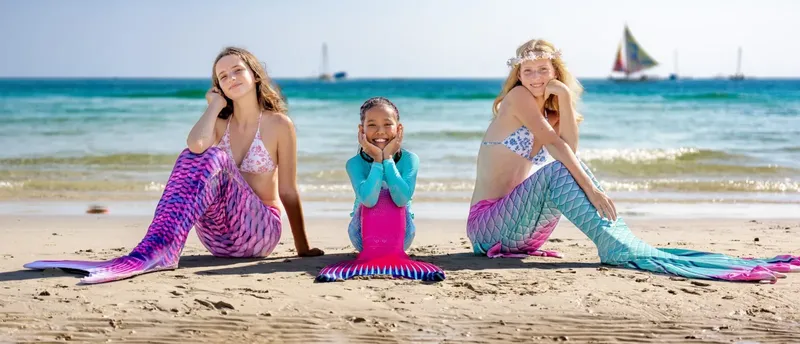 Trois personnes en costumes de sirène assises sur une plage