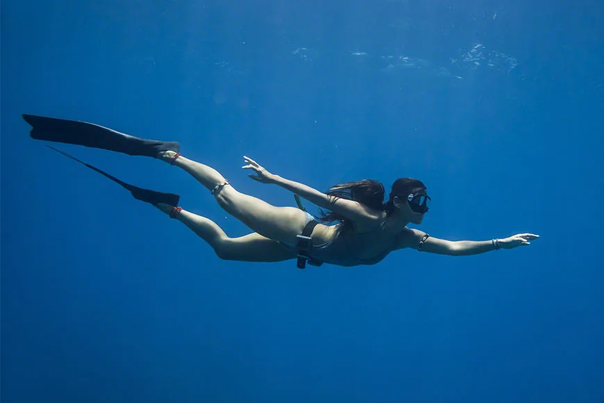 Apnée : une femme nage en apnée dans une eau bleue claire