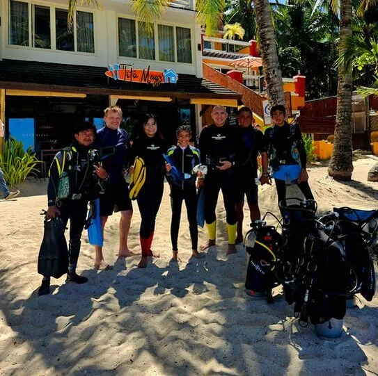 Groupe de plongeurs souriants sur une plage devant le centre