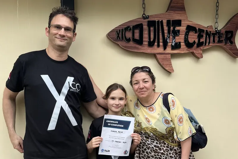 Quatre personnes souriantes posent devant l'enseigne d'un centre de plongée
