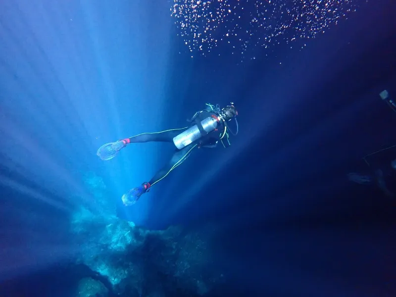 Plongeur en scaphandre nageant dans une eau bleue éclairée par le soleil