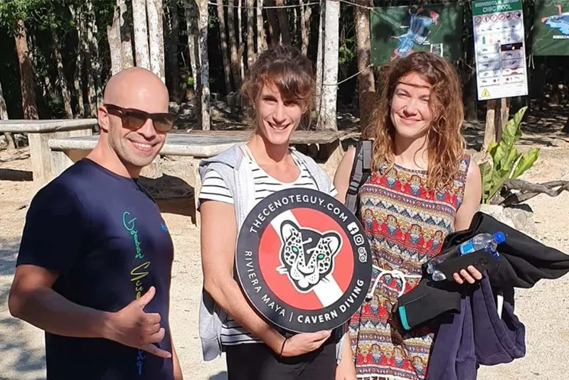 Trois personnes souriantes posent devant un logo de centre de plongée