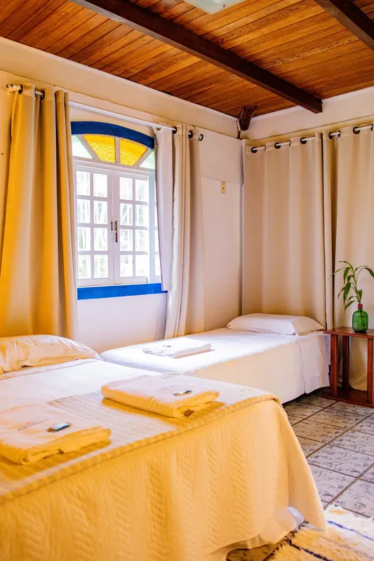 Chambre lumineuse avec deux lits simples, rideaux jaunes et vue sur l'extérieur