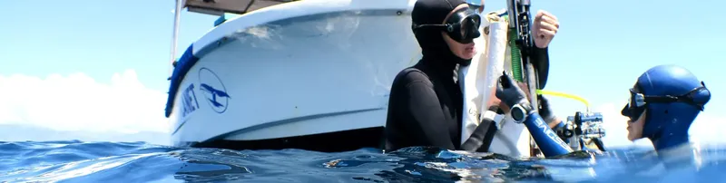 Plongeurs près d'un bateau, équipement visible, eau claire et ensoleillée