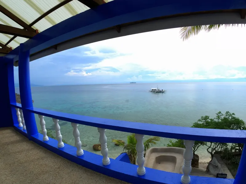 Vue sur la mer depuis une terrasse bleue avec un bateau au loin