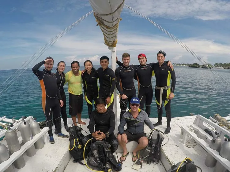 Groupe de plongeurs souriants sur un bateau en mer, équipement visible