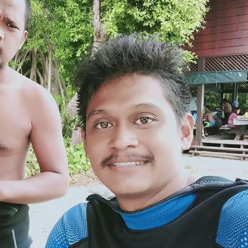 Deux hommes souriants, un en premier plan avec combinaison de plongée