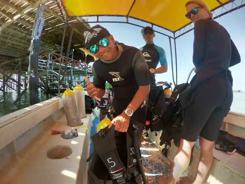 Plongeurs équipés sur un bateau, sourires et pouce levé au soleil
