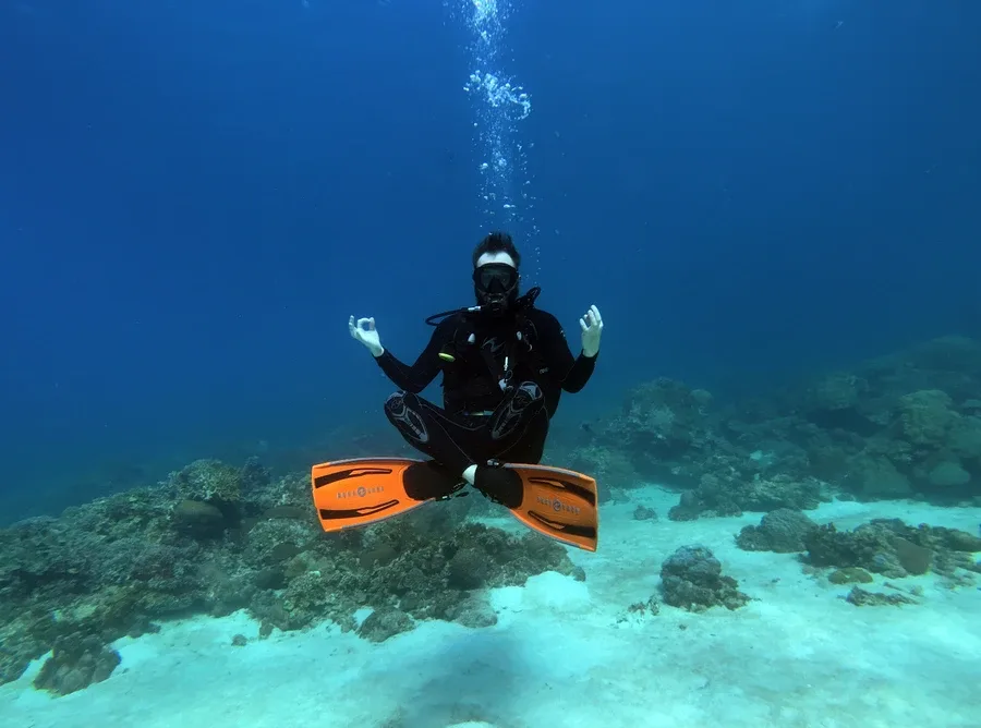 Plongeur en position de méditation sous l'eau, visage détendu, récif corallien