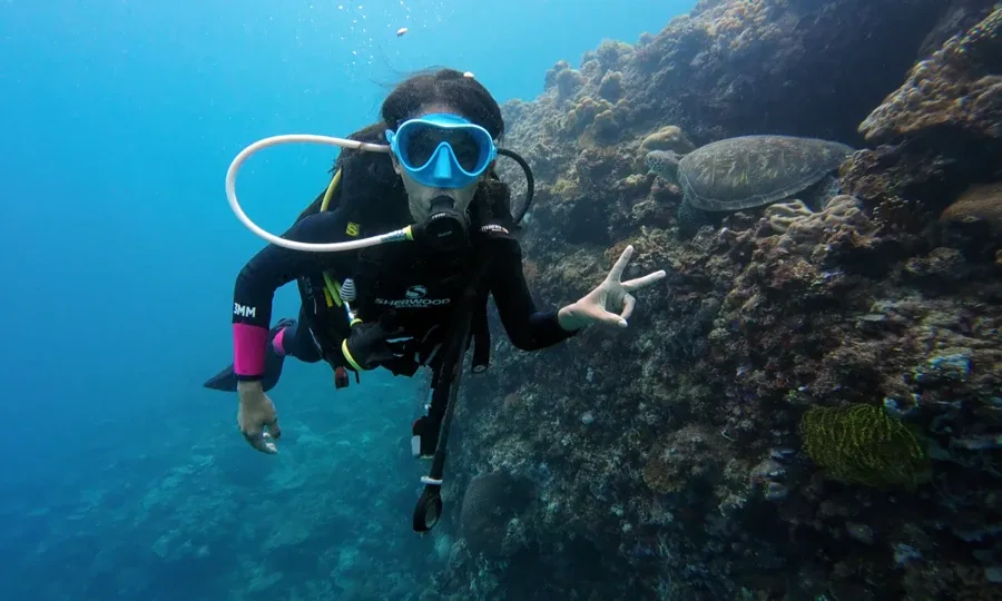 Plongeuse souriante face caméra avec tortue de mer en arrière-plan