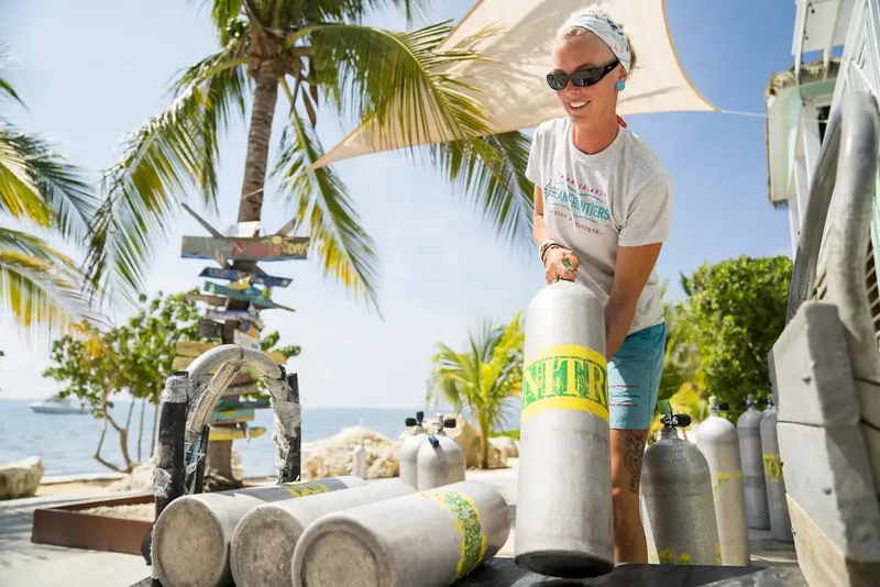 Femme souriante manipulant des bouteilles de plongée sur une plage ensoleillée