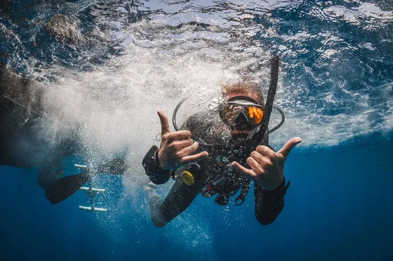 Plongeur souriant faisant le signe 'shaka' sous la surface de l'eau