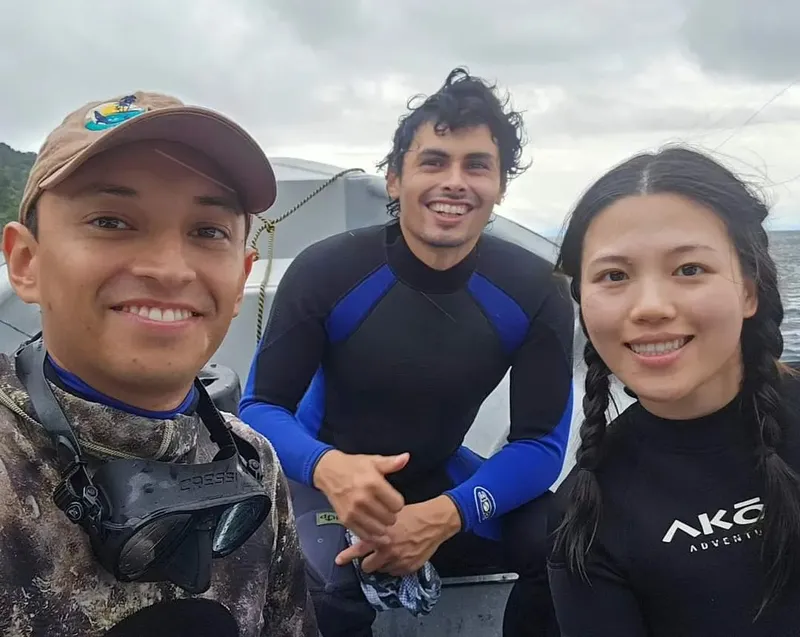 Trois personnes souriantes en combinaison de plongée sur un bateau
