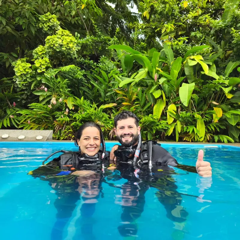 Deux plongeurs souriants en combinaison dans une piscine bleu clair