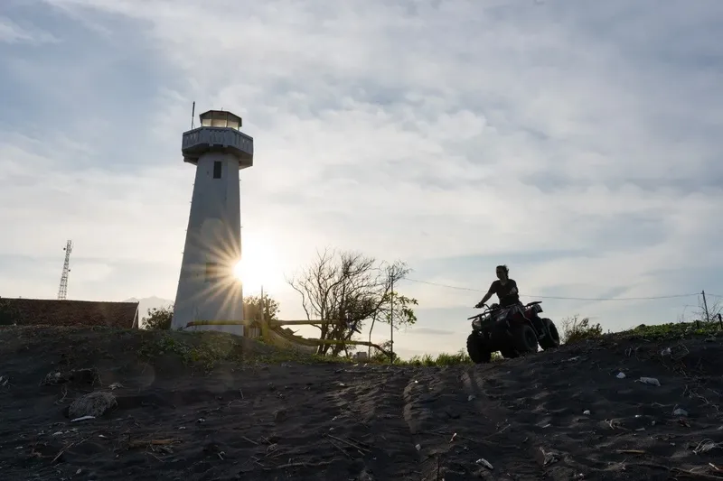 Personne conduisant un quad devant un phare et un ciel nuageux