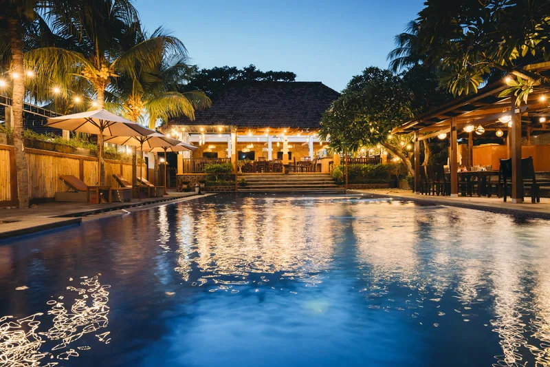 Piscine illuminée avec bâtiment en arrière-plan et végétation tropicale