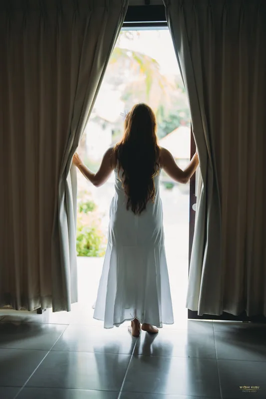 Femme en robe blanche regardant vers l'extérieur depuis une ouverture