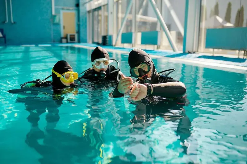 Trois plongeurs en formation dans une piscine, équipement complet visible