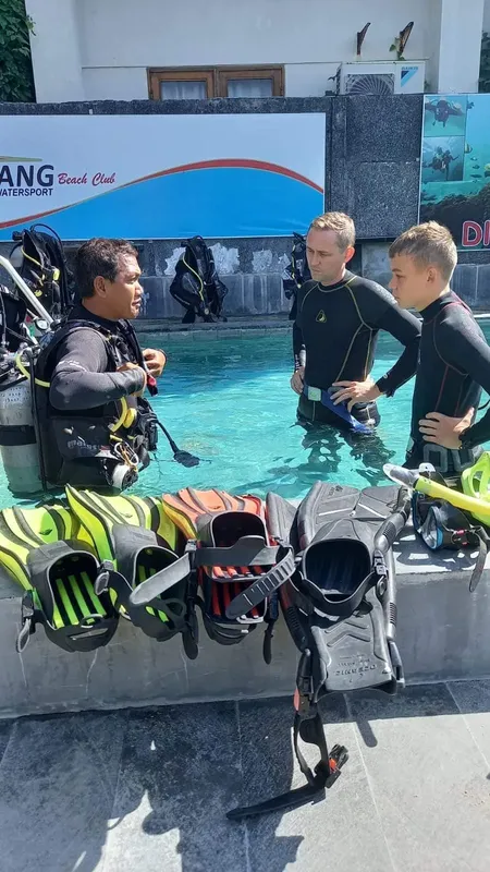 Trois personnes en combinaison de plongée discutent au bord d'une piscine