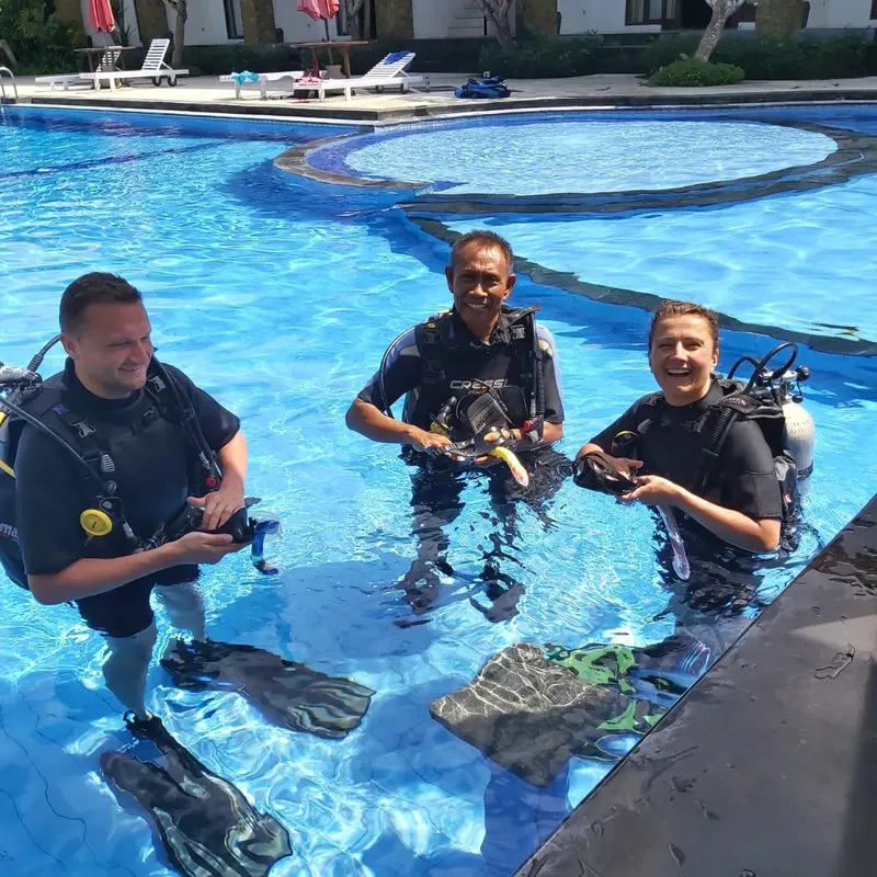Trois plongeurs souriants équipés dans une piscine ensoleillée