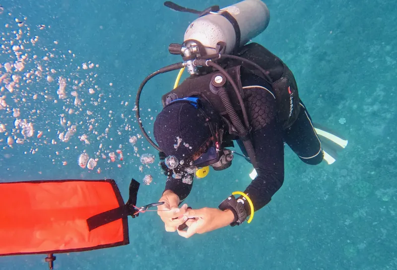 Plongeur en combinaison noire manipule un objet sous l'eau avec des bulles