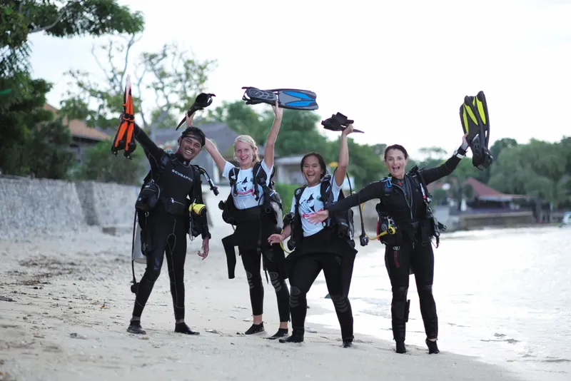 Groupe de plongeurs souriants sur une plage, équipement de plongée visible