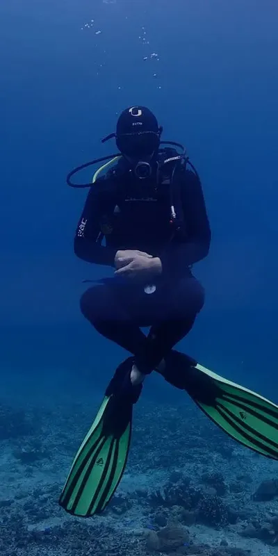 Plongeur en combinaison noire, jambes croisées, dans l'eau bleue