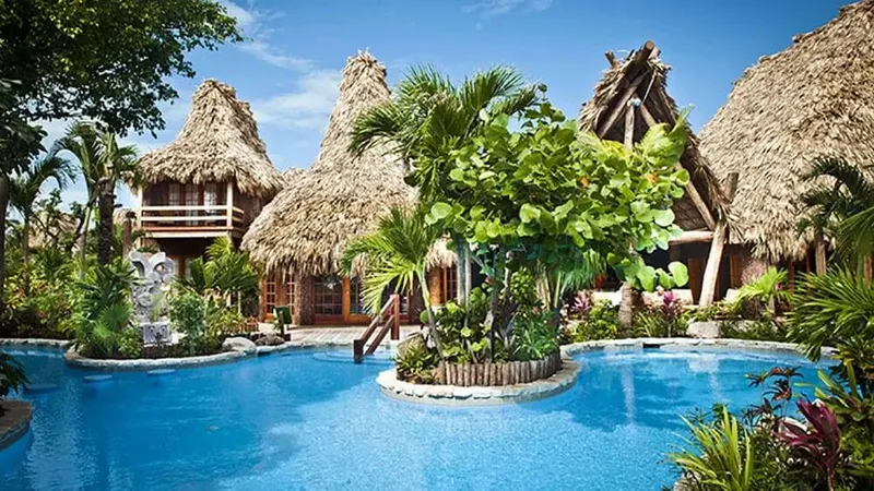 Bâtiments avec toits de chaume entourant une piscine tropicale luxuriante