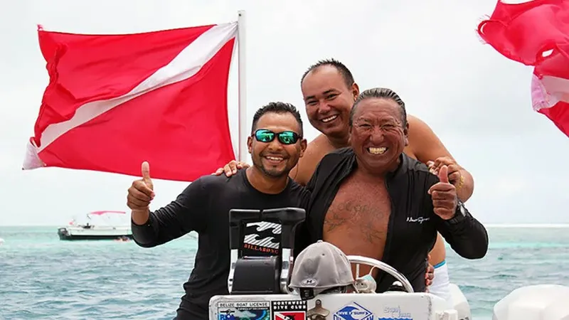 Trois hommes souriants sur un bateau avec un drapeau de plongee