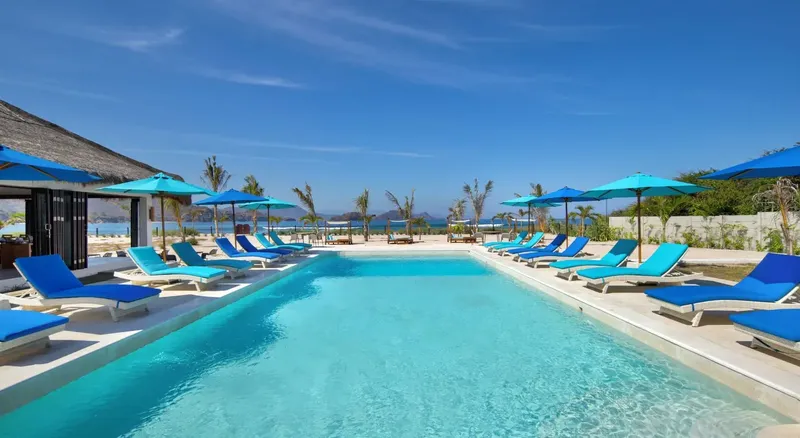Piscine bleue avec transats et parasols, vue sur la mer