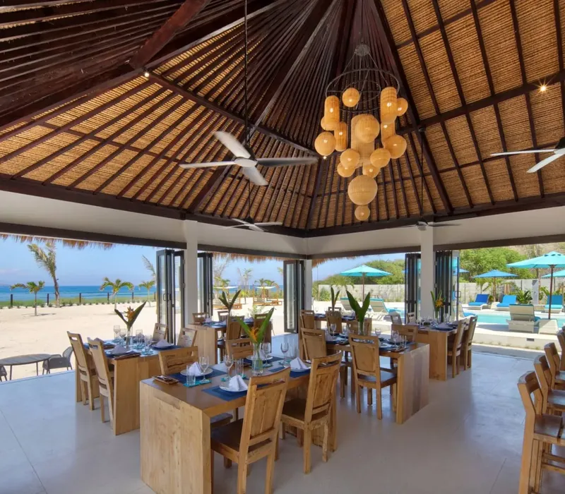 Salle à manger ouverte sur la plage avec tables et décoration tropicale