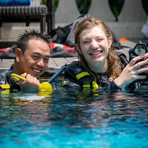 Deux plongeurs souriants dans une piscine avec leur équipement