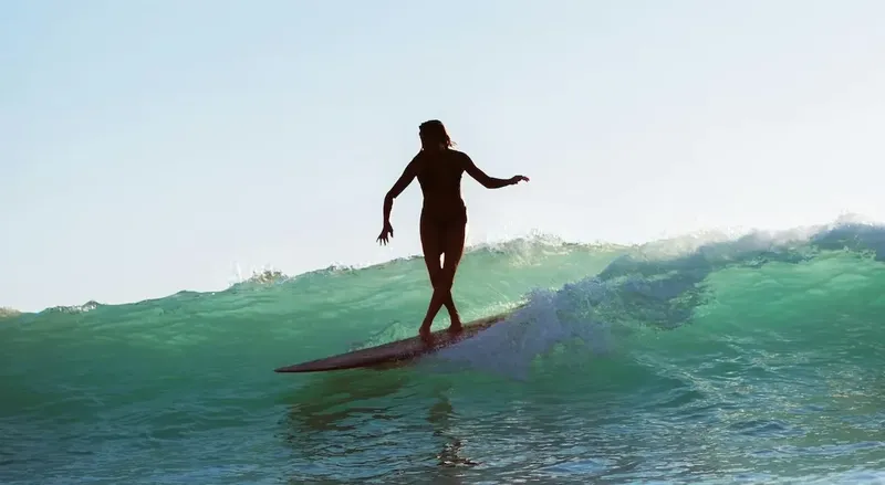 Silhouette d'une surfeuse sur une vague au lever du soleil