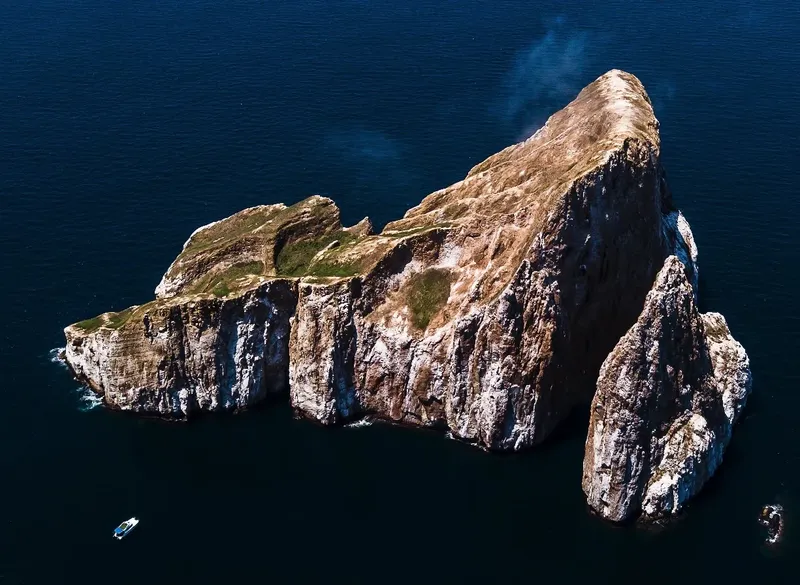 Île rocheuse escarpée entourée d'eau sombre avec un petit bateau