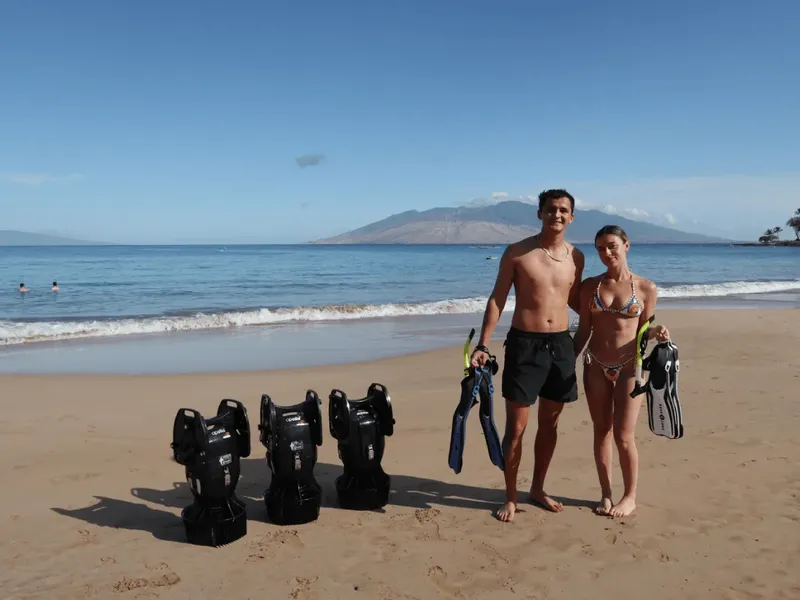Un couple de plongeurs souriants sur une plage avec du matériel