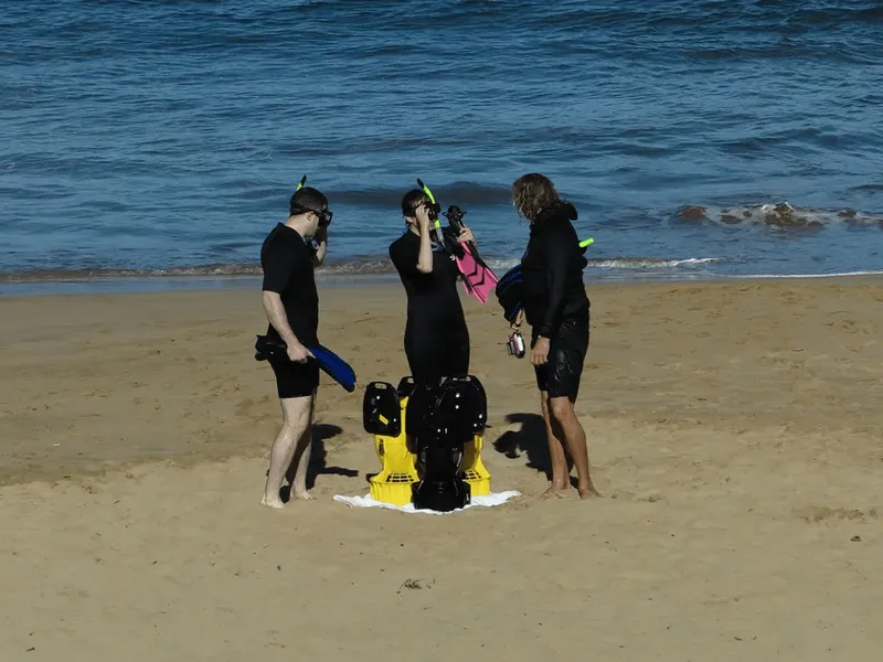 Trois plongeurs équipés sur une plage de sable ensoleillée