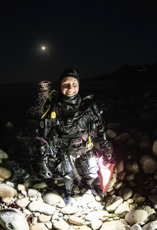 Plongeur souriant en combinaison complète sur un rivage rocheux nocturne