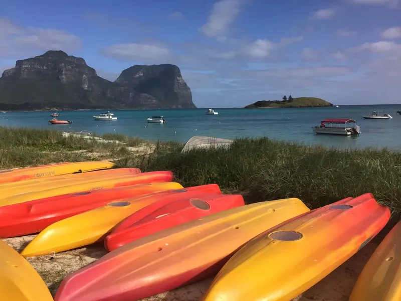 Plage avec kayaks, bateaux en mer et montagne en arrière-plan