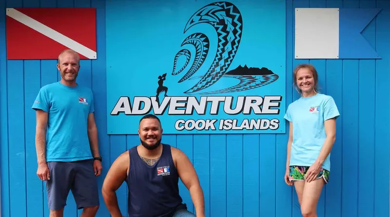 Trois personnes souriantes posent devant un mur bleu et un logo