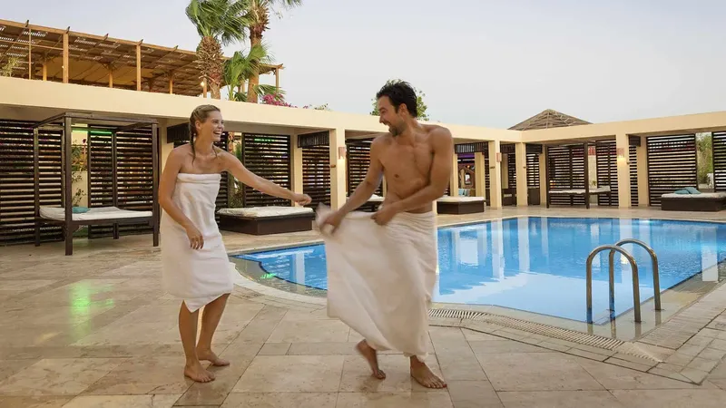Couple souriant en peignoir près d'une piscine ensoleillée et relaxante