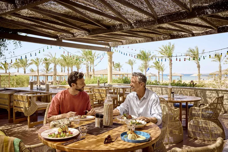 Deux hommes discutent en mangeant dans un restaurant en bord de mer