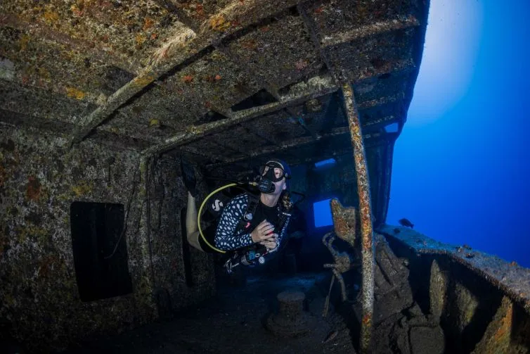 Plongeur explore l'épave d'un navire, lumière bleue ambiante