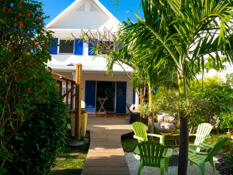 Façade d'un bâtiment blanc avec végétation tropicale et mobilier extérieur vert
