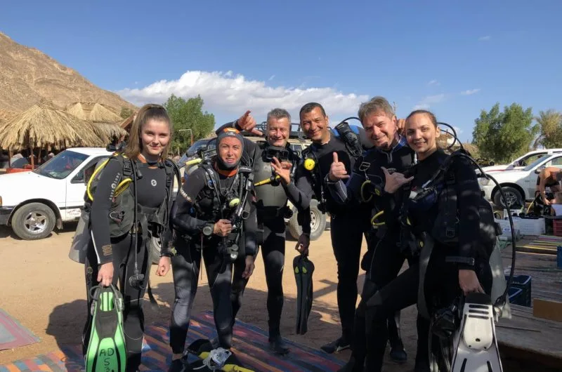Groupe de plongeurs souriants équipés sur un fond désertique ensoleillé