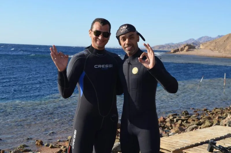 Deux plongeurs en combinaison souple sourient et font un signe de la main