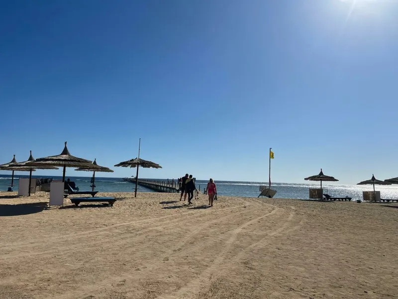 Plage de sable avec parasols, personnes marchant vers un ponton